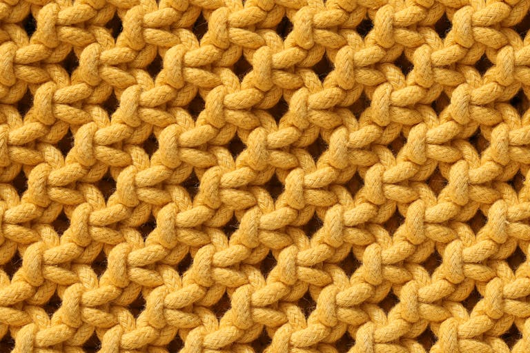 Detailed close-up view of vibrant yellow knitted fabric texture, showcasing intricate patterns.