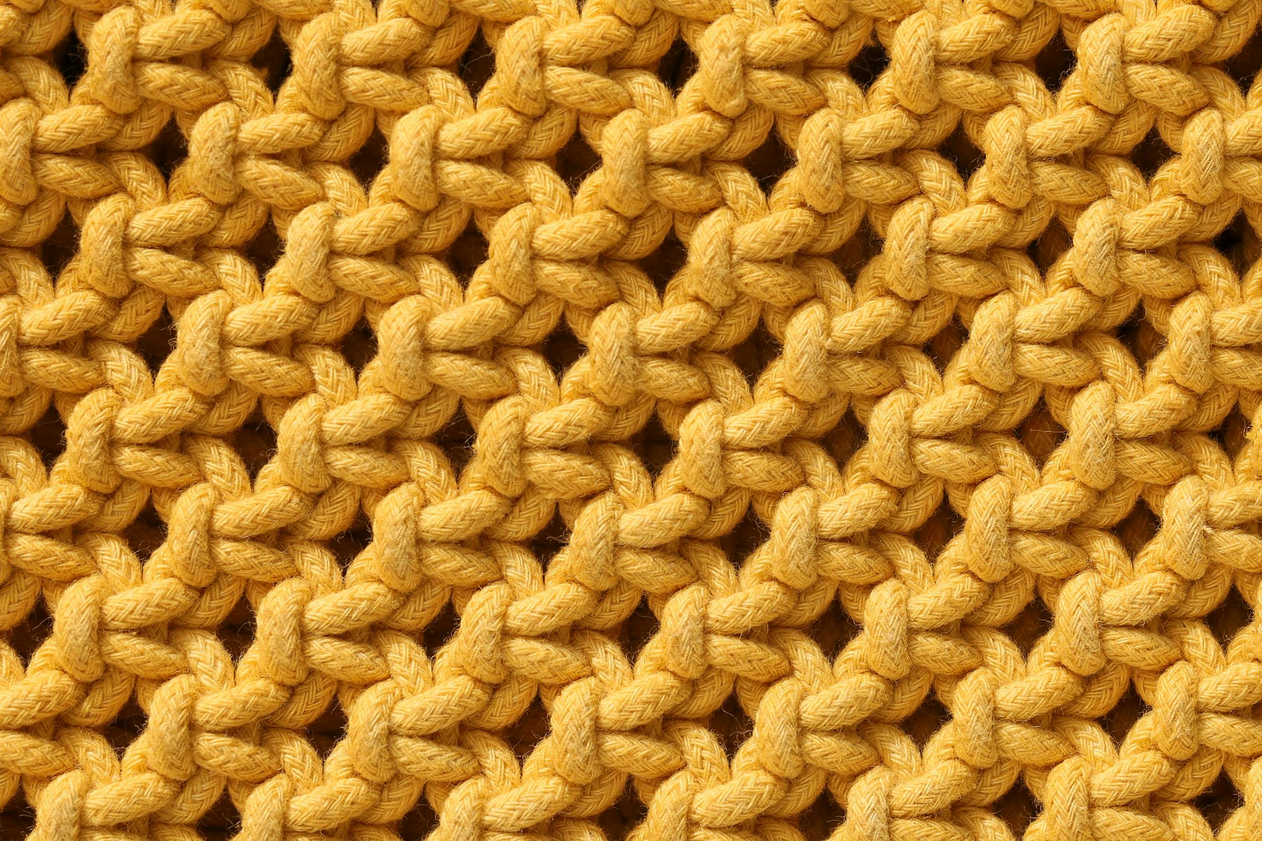 Detailed close-up view of vibrant yellow knitted fabric texture, showcasing intricate patterns.